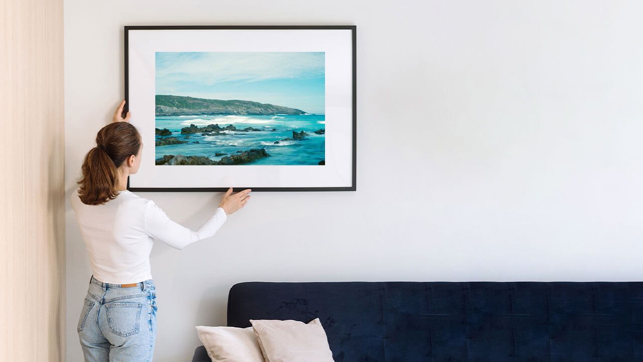 Person hanging art above couch
