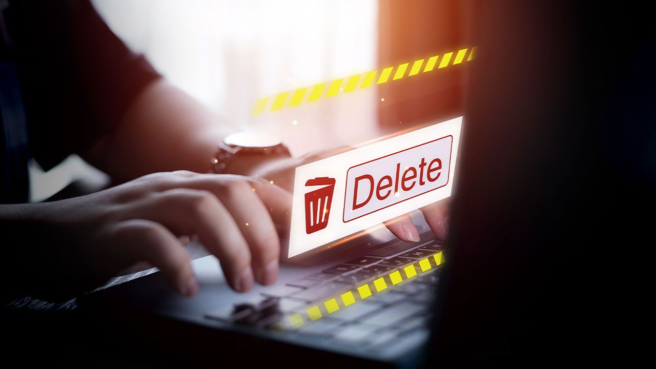 Hands typing on a laptop keyboard with a glowing "Delete" button icon displayed on the screen.