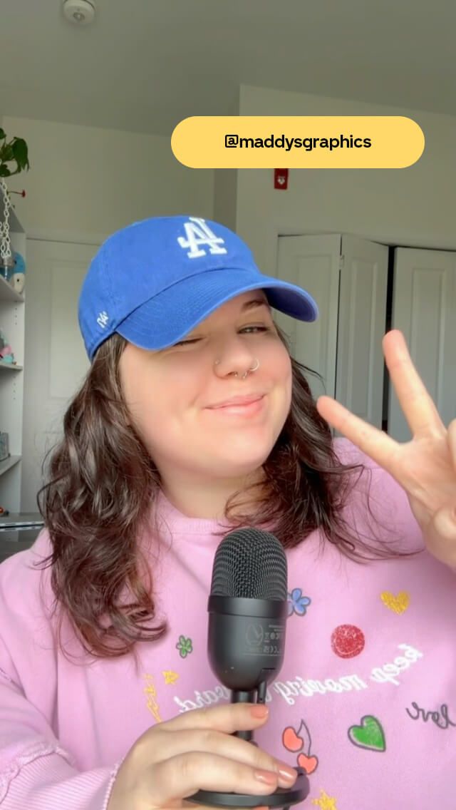 Person in a pink sweater and blue cap holding a microphone, making a peace sign. Text overlay: "@maddysgraphics".