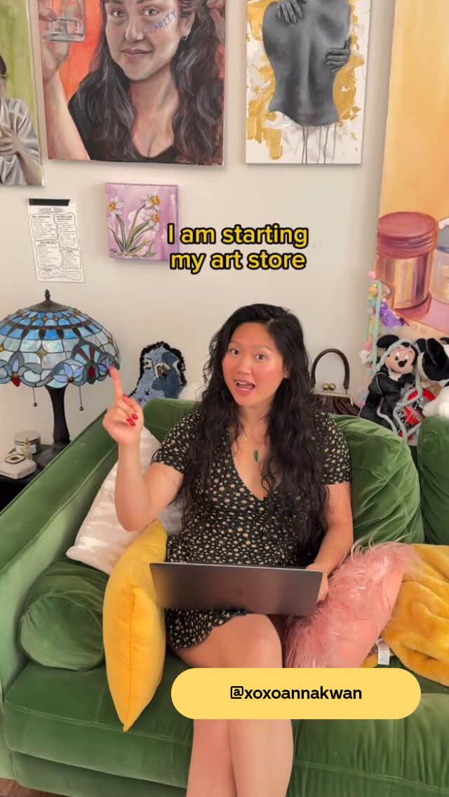 Woman sitting on a green couch with a laptop, pointing up. Text reads, "I am starting my art store." Artworks displayed on the wall.