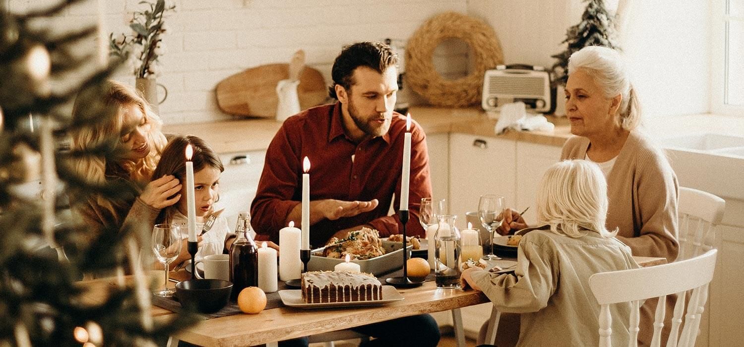 A family gathered around a dining table, enjoying a meal with candles and festive decorations in a cozy kitchen setting.