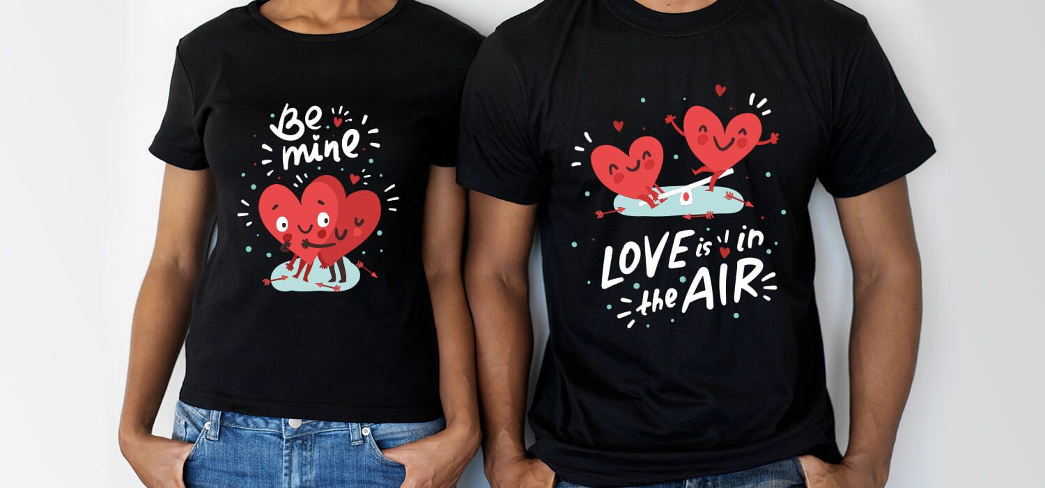 Two people wearing black T-shirts with heart designs. One shirt says "Be Mine," and the other says "Love is in the Air."